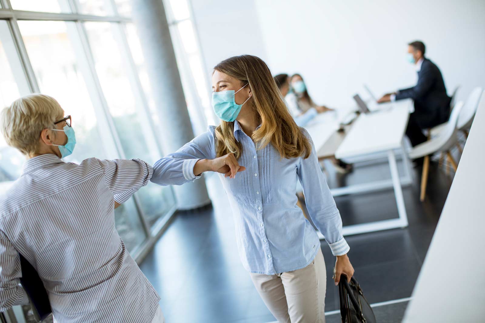 Two business women in covid masks shaking hands in a meeting room