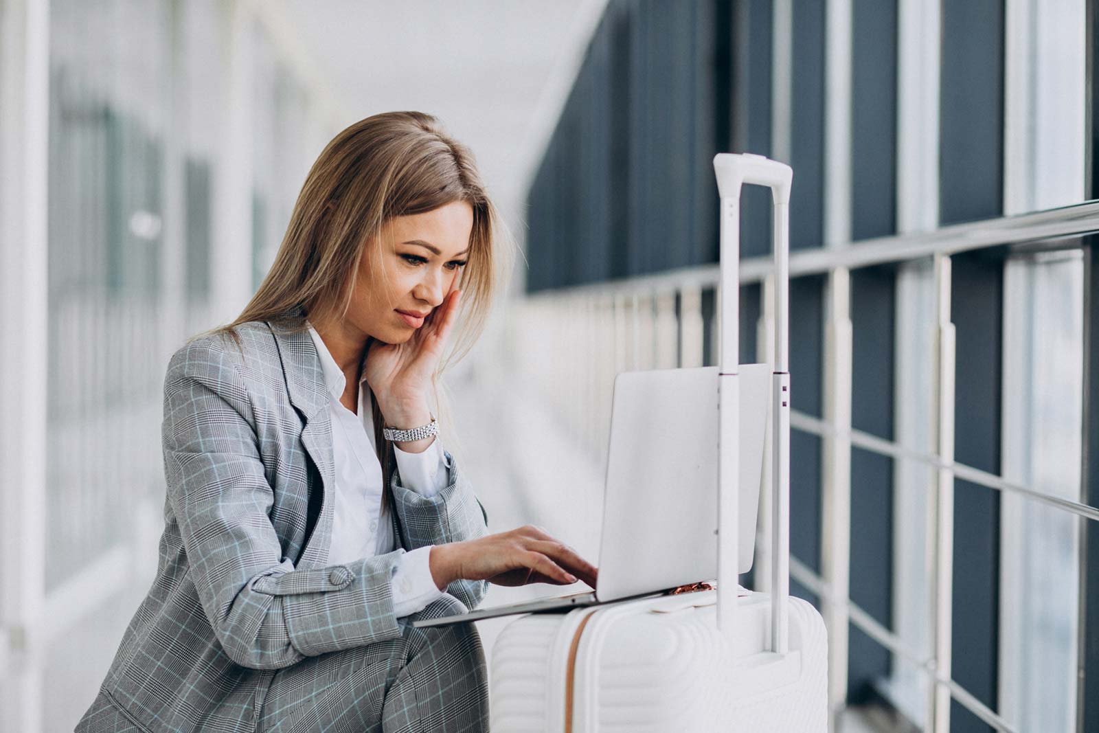 Mulher de negócios com uma mala de viagem, reservando um voo no laptop no aeroporto