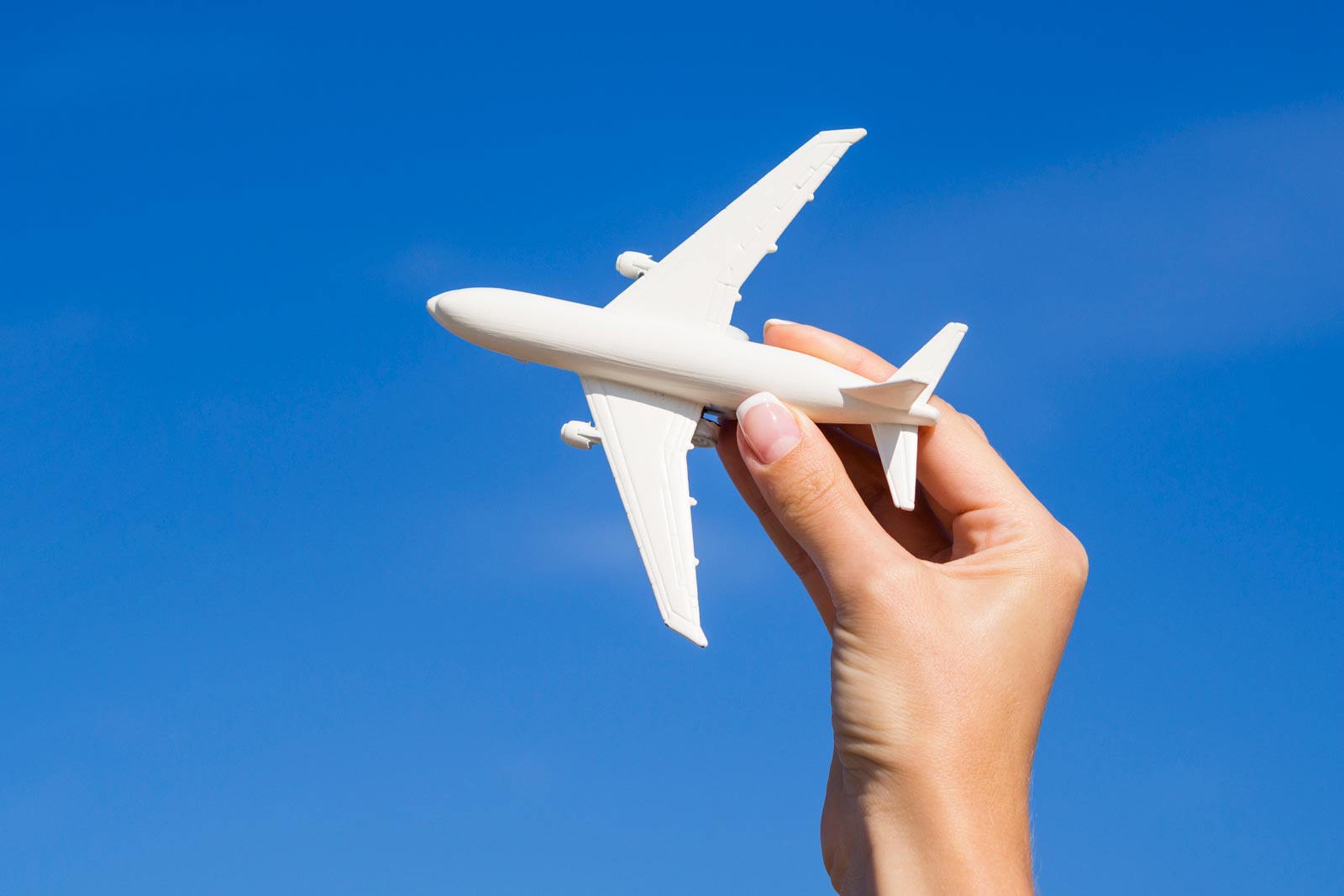 Female hand holding an airplane model, on a blue sky