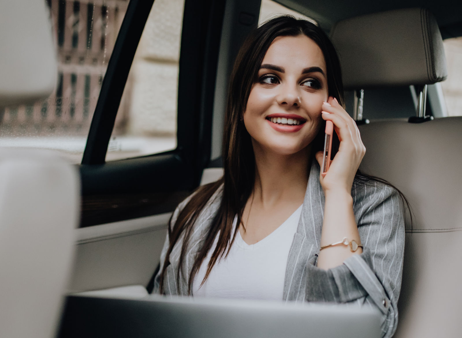 Mulher de negócios dentro de um taxi a usar o telemóvel e o computador portátil